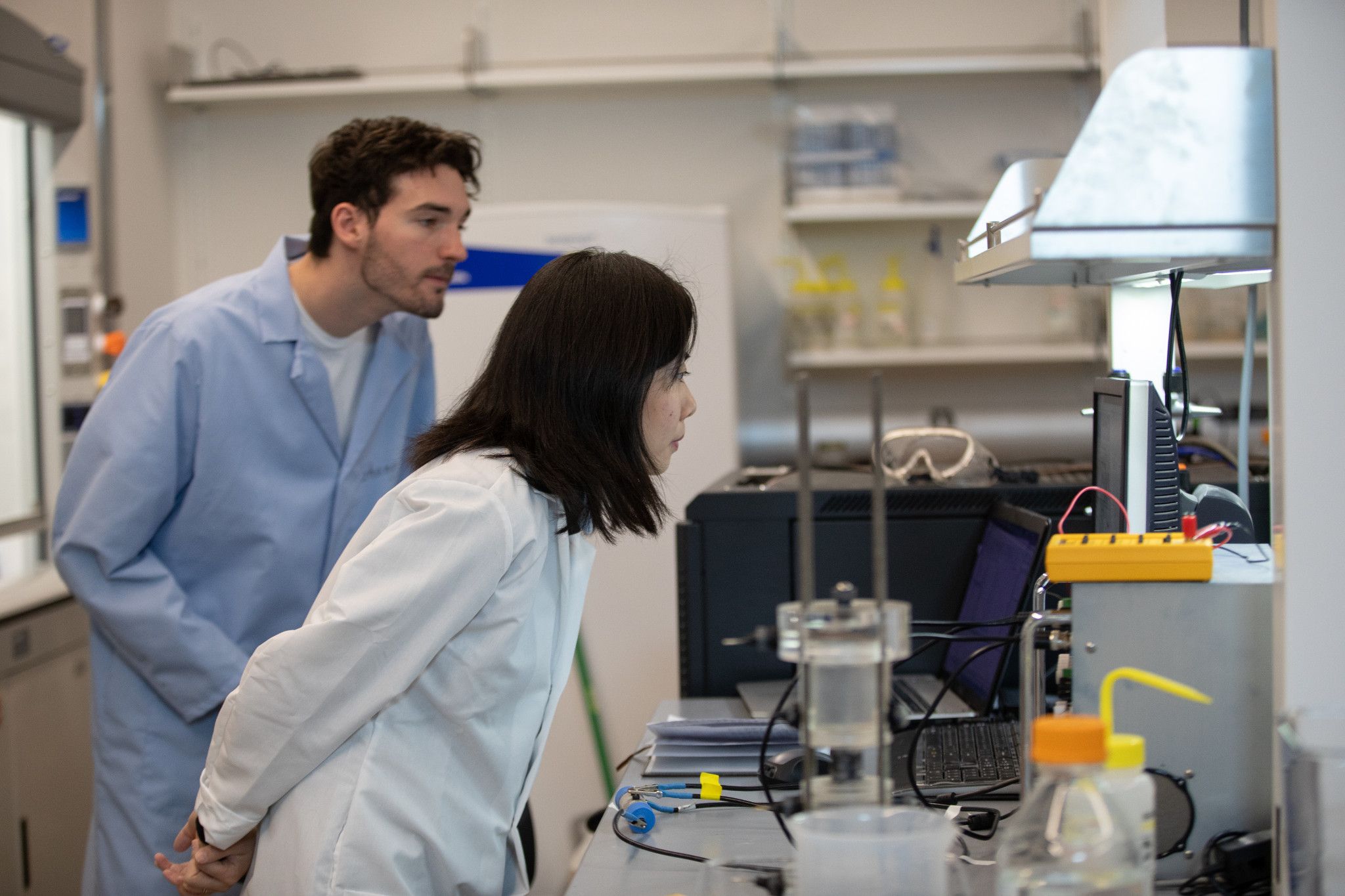 Student and professor lean towards computer screen in a geology research lab.